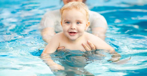 Kızıl saçlı küçük bir çocuğun portresi bahçede açık havuzda el desteği ile yıkanır, bebek suda oynar, aile yaz tatili yapar.