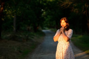 Genç kadın ağaçların arasında tek başına ayakta duruyor. Elleri doğa üzerinde dua ediyor. Tanrı 'ya şükür ki, karanlıkta gün ışığıyla aydınlanıyor.