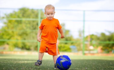 Futbol sahasında oynayan iki yaşında bir çocuk, top oynayan küçük bir çocuk, aktif yaz tatili ve spor konsepti.