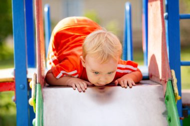 Parkta yürüyen sevimli küçük bir çocuk, çocuk oyun parkındaki kaydırağın üzerine tırmandı, eğlence aktivitesi konsepti.