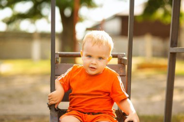 Parkta salıncakta sallanan sevimli sarışın çocuk, doğada çocukla vakit geçiriyor.