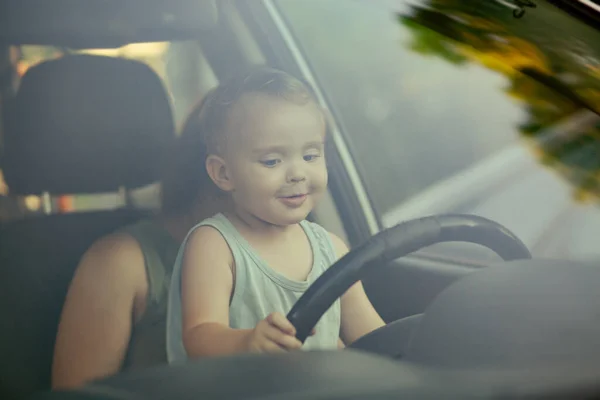 車の中で母親の膝の上に座ってステアリングホイールを回す子供 楽しい 家族のコンセプトのための小さなかわいいブロンドの少年ドライブ車 — ストック写真