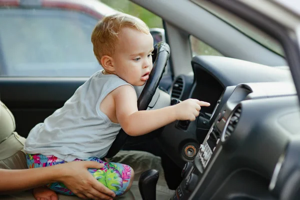 車の母親の膝の上に座っている子供 かわいい少年は楽しみを持っています ステアリングホイールの頬に横たわり コントロールボタン 家族の概念を押します — ストック写真