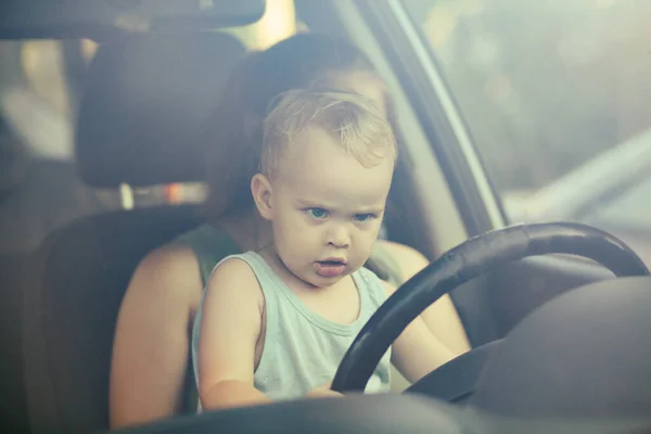 車の中で母親の膝の上に座ってステアリングホイールを回す子供 楽しい 家族のコンセプトのための小さなかわいいブロンドの少年ドライブ車 — ストック写真