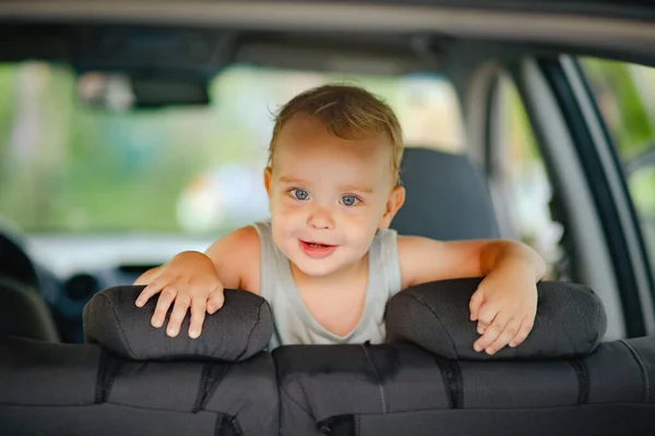 一个金发碧眼的小男孩在车舱里玩耍 躲在后排的行李箱里 看着外面 童年时代的快乐 — 图库照片