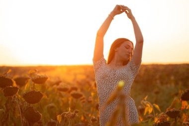 Genç bir kadın güneş ışığında yaz günbatımında bir çiçek tarlasında ellerini havada tutan bir kız, doğa kavramında gevşeme.