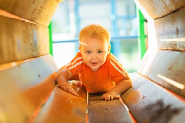 Parktaki parkta yürüyen sevimli sarışın çocuk, eğlence borularından geçen çocuk kremleri, eğlence aktivitesi konsepti.
