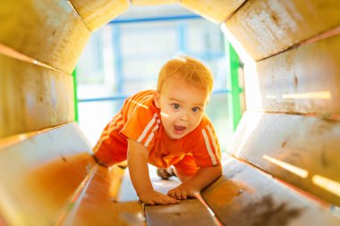 Parktaki parkta yürüyen sevimli sarışın çocuk, eğlence borularından geçen çocuk kremleri, eğlence aktivitesi konsepti.