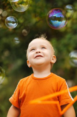 Mutlu küçük çocuğun portresi doğada sabun köpüklerine bakıyor, gülümseyen bebek yüzü, çocukluk ve eğlence kavramı