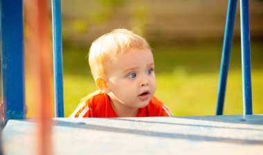 Parkta yürüyen sevimli küçük bir çocuk, çocuk oyun parkındaki kaydırağın üzerine tırmandı, eğlence aktivitesi konsepti.