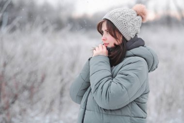 Şapkalı genç ve güzel bir kadın ellerini nefesiyle ısıtıyor. Soğuk bir günde yürüyen tatlı bir kız. Kış yürüyüşü.