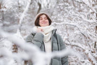 Kışın ağaçların dalları arasında karla kaplı güzel genç bir kadın. Karlı ormanda yürüyen güzel bir kız.