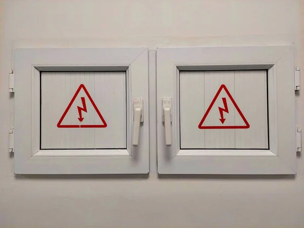 Two small doors guard the power grid. On the door is a lightning symbol in a triangle. The warning sign is electrical voltage. Danger of Electric Shock High Voltage Sign Isolated Triangle.