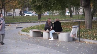 Ukrayna, Harkiv, 27 Ekim 2021. Şehirdeki hayat. Kasabanın merkezinde sonbahar günü. Parktaki bankta iki kız konuşuyor. Yüksek kalite 4k görüntü