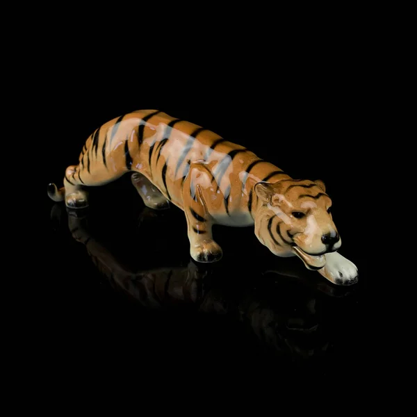 Tiger statuette isolated on a black background with reflection. antique porcelain figurine of a tiger