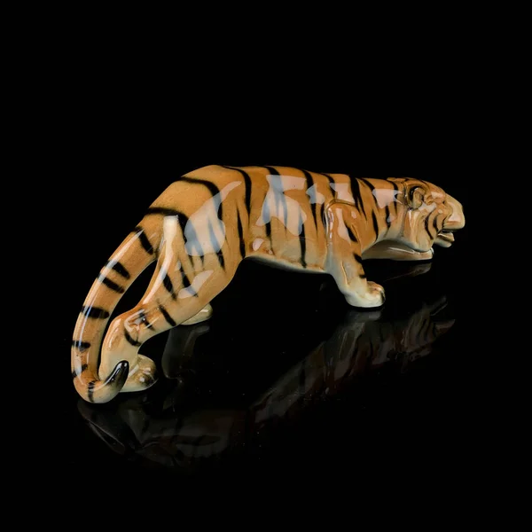 Tiger statuette isolated on a black background with reflection. antique porcelain figurine of a tiger