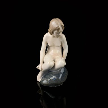Statuette of a girl on a black background with reflection. porcelain antique figurine of a mermaid sitting on a stone
