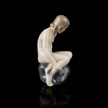 Statuette of a girl on a black background with reflection. porcelain antique figurine of a mermaid sitting on a stone