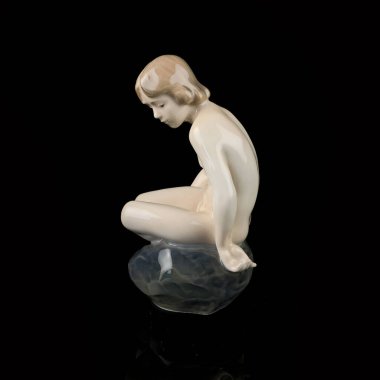 Statuette of a girl on a black background with reflection. porcelain antique figurine of a mermaid sitting on a stone