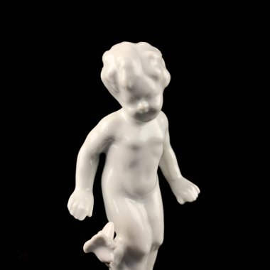 Plastic figurine of a man with a golden ball on a black background. porcelain antique figurine of a boy
