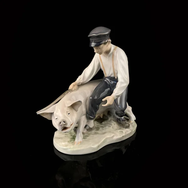 Ceramic figurine of a man and a pig on a black background.  porcelain antique figurine of a boy