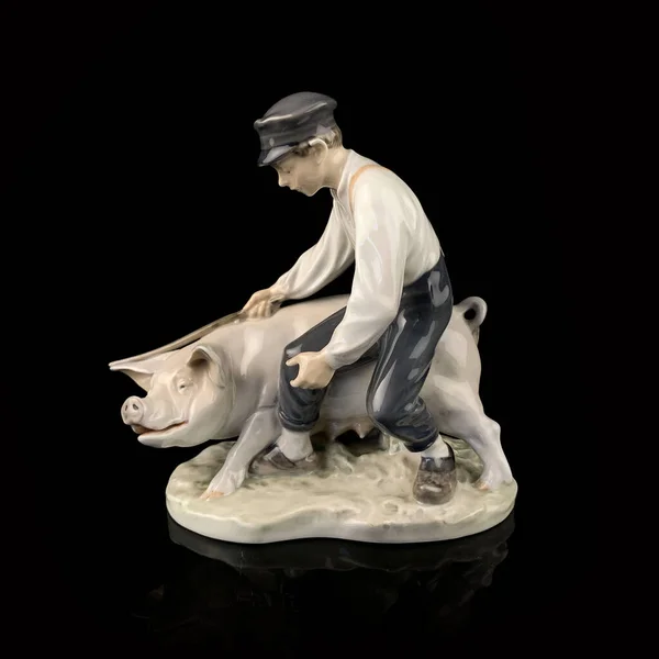 Ceramic figurine of a man and a pig on a black background.  porcelain antique figurine of a boy