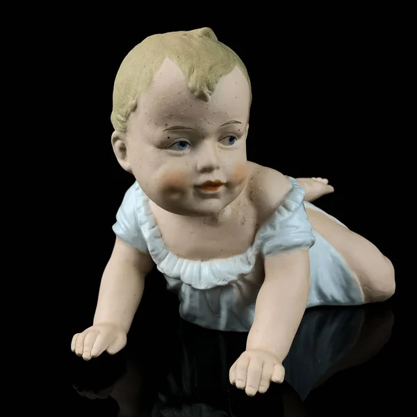 Cute little baby doll isolated on black background with reflection in water. antique figurine of a baby. toy baby