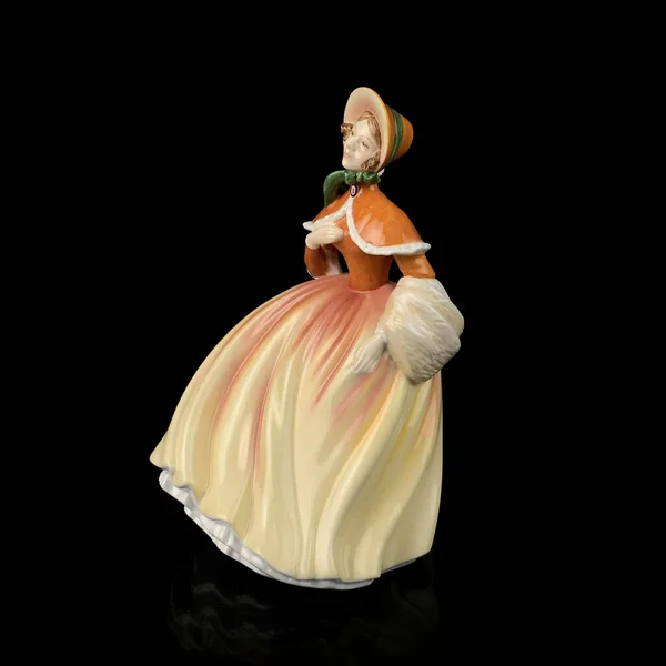 Statuette of a woman in an orange dress and hat on a black background. vintage figurine of a woman in a retro dress. the dress moves with the wind.