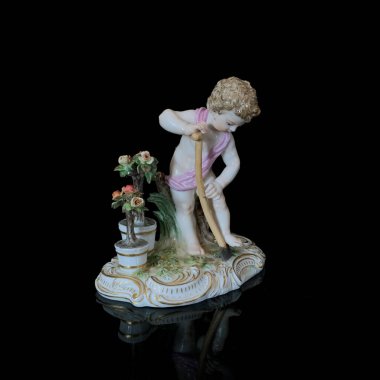 Ceramic statuette of an angel on a black background. old figurine of a boy in a flower garden.