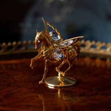 antique gold figurine of a horse in a luxurious interior. golden pegasus on a dark background close-up, macro photography