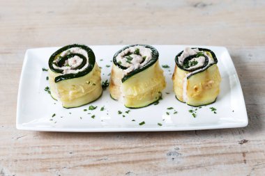 Grilled zucchini rolls stuffed with cream cheese and tuna on wooden table