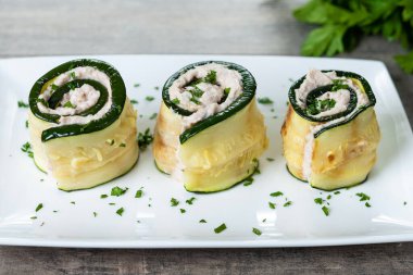 Grilled zucchini rolls stuffed with cream cheese and tuna on wooden table