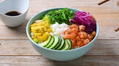man eating poke bowl with chopsticks on wooden table 