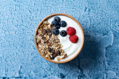 Yogurt with berries and muesli for breakfast in bowl on lbue background. Top view