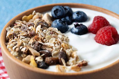 Yogurt with berries and muesli for breakfast in bowl on lbue background. Close up