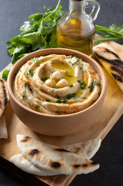Chickpea hummus in a wooden bowl garnished with parsley, paprika and olive oil on black background