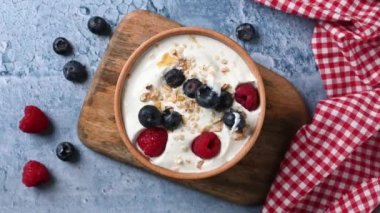 Throwing berries at yogurt for breakfast in bowl on blue background. Top view