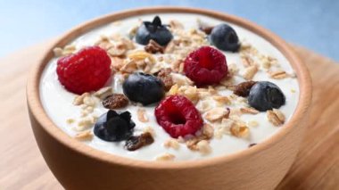 Yogurt with berries and muesli for breakfast in bowl circling on blue background