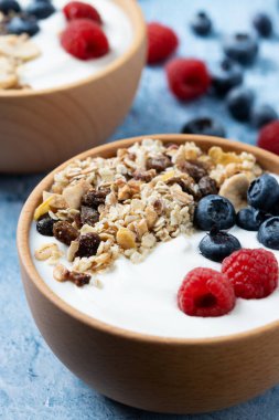 Yogurt with berries and muesli for breakfast in bowl on blue background. Close up