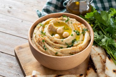 Chickpea hummus in a wooden bowl garnished with parsley, paprika and olive oil isolated on white background