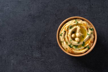 Siyah arka planda maydanoz, kırmızı biber ve zeytinyağıyla süslenmiş ahşap bir kasede nohut. Üst Manzara. Boşluğu kopyala