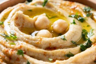 Chickpea hummus in a wooden bowl garnished with parsley, paprika and olive oil. Close up