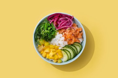 Pirinç, somon, salatalık, mango, soğan, wakame salatası, haşhaş tohumu ve sarı arka planda izole ayçiçeği çekirdekleri.