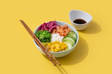 Pirinç, somon, salatalık, mango, soğan, wakame salatası, haşhaş tohumu ve sarı arka planda izole ayçiçeği tohumlarıyla karıştırın..