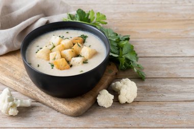 Tahta masadaki bir kasede karnabahar çorbası. Boşluğu kopyala