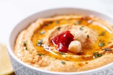 Beyaz mermer arka planda kavrulmuş kırmızı biberli humus. Kapat.