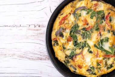 Beyaz ahşap masada ıspanak, domates, soğan ve biberden yapılmış İtalyan Frittata. Üst Manzara. Boşluğu kopyala
