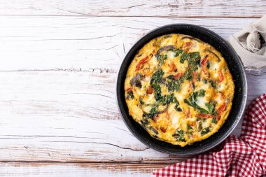 Beyaz ahşap masada ıspanak, domates, soğan ve biberden yapılmış İtalyan Frittata. Üst Manzara. Boşluğu kopyala
