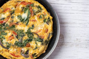 Beyaz ahşap masada ıspanak, domates, soğan ve biberden yapılmış İtalyan Frittata. Üst Manzara. Boşluğu kopyala