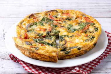 Beyaz ahşap masada ıspanak, domates, soğan ve biberden yapılmış İtalyan Frittata.